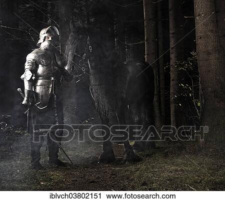 Stock Image - "Knight wearing armour standing beside his horse in the woods, Tyrol, Austria, Europe". Fotosearch
