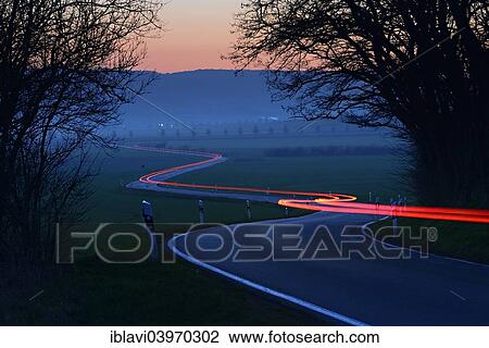 Stock Image - "Light trails on a winding country road, night shot, long exposure, Saxony-Anhalt, Germany, Europe". Fotosearch