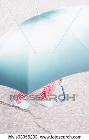 Stock Image - "Little girl with dotted pants under big umbrella, Sweden, Europe". Fotosearch