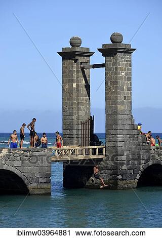 "Local children and young people bathing at the Puente de las Bolas, stone gate outside the fort Castillo de San Gabriel, Arrecife, Lanzarote, Canary Islands, Spain, Europe" View Large Photo Image Stock Image - "Local children and young people bathing at the Puente de las Bolas, stone gate outside the fort Castillo de San Gabriel, Arrecife, Lanzarote, Canary Islands, Spain, Europe". Fotosearch