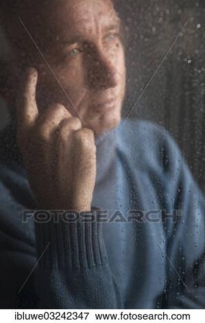 Stock Photo - "Lonely man sitting behind a window covered in rain drops, Mannheim, Baden-Wurttemberg, Germany, Europe". Fotosearch