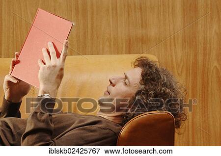 Stock Photo - "Man, 30-40, lying on a sofa, reading a red book". Fotosearch