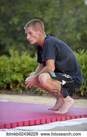"Man, 40-50 years old, squatting barefoot on a sports mat in a park" View Large Photo Image Stock Photo - "Man, 40-50 years old, squatting barefoot on a sports mat in a park". Fotosearch
