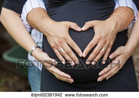 Man and a pregnant woman forming a heart shape with their hands on her belly View Large Photo Image Stock Image - Man and a pregnant woman forming a heart shape with their hands on her belly. Fotosearch