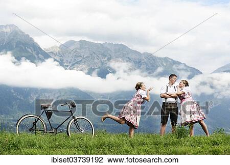 Stock Image - "Man and a woman wearing traditional costume with an old bicycle within a natural landscape, photocomposing, Aldrans, Tyrol, Austria, Europe". Fotosearch