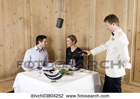 Stock Image - "Man and woman in a restaurant waited on by a waiter, Regensburg, Bavaria, Germany, Europe". Fotosearch