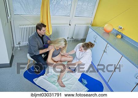 Stock Image - "Man and woman in the delivery room during childbirth, the woman is sitting on a birth stool during labour and is being supported by her midwife, Germany, Europe". Fotosearch