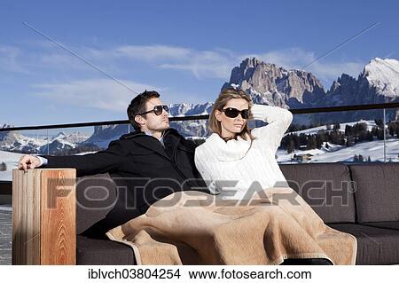 Picture - "Man and woman sitting on a couch outdoors, Seiser Alm, South Tyrol, Italy, Europe". Fotosearch