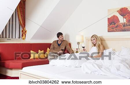 Stock Image - Man and woman with a glass of red wine in a bedroom of a hotel. Fotosearch