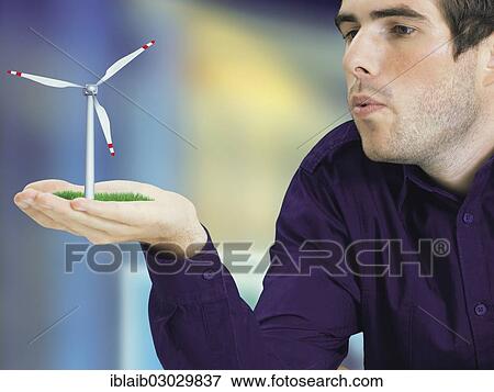 Stock Photo - Man blowing a miniature wind turbine in his hand. Fotosearch