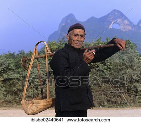 Stock Image - "Man carrying a load with a shoulder pole in front of Moon Mountain near Yangshuo, Guilin, Guangxi, China, Asia". Fotosearch