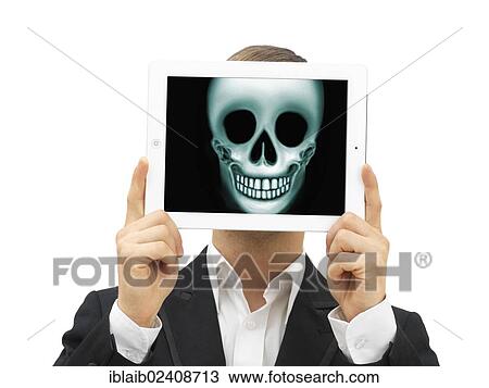 Stock Image - Man holding an iPad with a skull in front of his face. Fotosearch