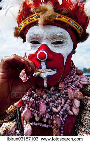 Stock Image - "Man in a colourfully decorated costume with face paint smoking a cigarette at the traditional sing-sing gathering, Hochland, Mount Hagen, Western Highlands Province, Papua New Guinea, Oceania". Fotosearch