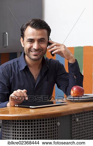 Picture - Man in the kitchen with a mobile phone and an iPad. Fotosearch