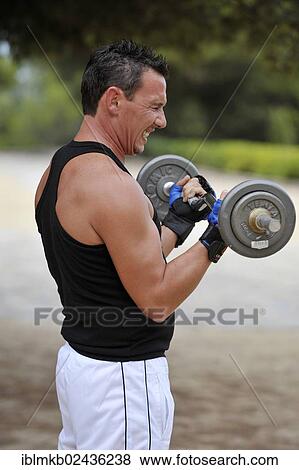 Man lifting weights while exercising in a park View Large Photo Image Stock Photo - Man lifting weights while exercising in a park. Fotosearch