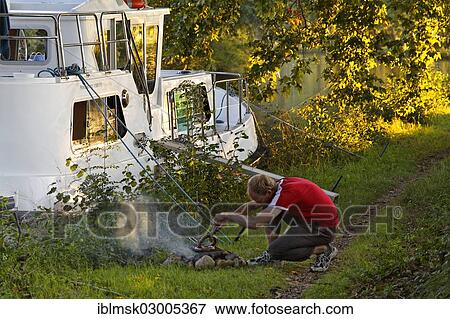 "Man making a fire to grill for dinner, beside a houseboat on the Canal du Midi, at Ecluse de l'Ocean lock, Pk 51. 6, Avignonet-Lauragais, Midi-Pyrenees, France, Europe" View Large Photo Image Stock Photo - "Man making a fire to grill for dinner, beside a houseboat on the Canal du Midi, at Ecluse de l'Ocean lock, Pk 51. 6, Avignonet-Lauragais, Midi-Pyrenees, France, Europe". Fotosearch