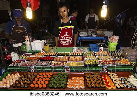 Stock Image - "Man selling sushi at a stand in the Night Market in Walking Street, Chiang Rai, Chiang Rai Province, Northern Thailand, Thailand, Asia". Fotosearch