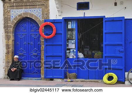 "Man sitting in front of a blue door next to a hardware store, Essaouira, Morocco, Africa" View Large Photo Image Stock Photo - "Man sitting in front of a blue door next to a hardware store, Essaouira, Morocco, Africa". Fotosearch
