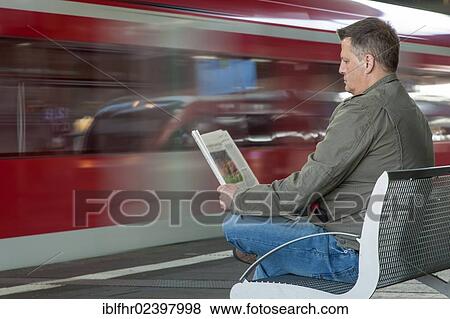 "Man sitting on a bench at a station reading a newspaper, Duesseldorf, North Rhine-Westphalia, Germany, Europe" View Large Photo Image Stock Photo - "Man sitting on a bench at a station reading a newspaper, Duesseldorf, North Rhine-Westphalia, Germany, Europe". Fotosearch