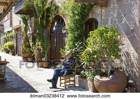 Stock Image - "Man sitting on a chair in front of a hotel, Assos, Canakkale Province, Marmara Region, Turkey, Asia". Fotosearch