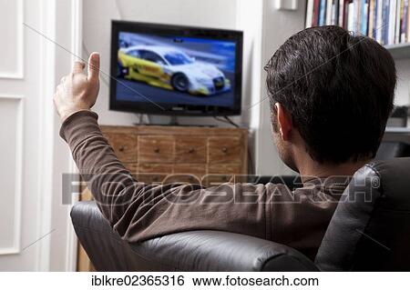 Man sitting on a leather sofa in front of a TV watching motorsport View Large Photo Image Stock Photograph - Man sitting on a leather sofa in front of a TV watching motorsport. Fotosearch