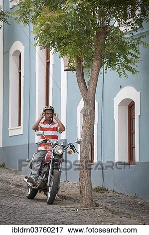 Stock Photo - "Man sitting on a motorcycle, Sao Filipe, Fogo Island, Cape Verde, Africa". Fotosearch
