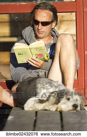 "Man sitting on a pier in the sun and reading a book with his dog sleeping in front of him, Weissensee lake, Carinthia, Austria, Europe" View Large Photo Image Stock Photograph - "Man sitting on a pier in the sun and reading a book with his dog sleeping in front of him, Weissensee lake, Carinthia, Austria, Europe". Fotosearch