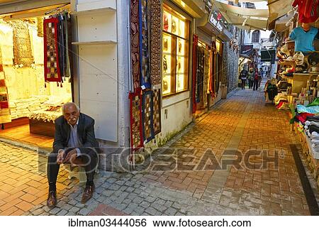 "Man sitting outside a carpet shop in the Bazaar of Kusadasi, Kusadasi, Aydin province, Aegean region, Turkey, Asia" View Large Photo Image Stock Photograph - "Man sitting outside a carpet shop in the Bazaar of Kusadasi, Kusadasi, Aydin province, Aegean region, Turkey, Asia". Fotosearch