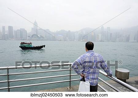"Man standing at the waterfront in Tsim Sha Tsui, Kowloon, looking at the Victoria Harbour and Hong Kong Island, Hong Kong, China, Asia" View Large Photo Image Stock Image - "Man standing at the waterfront in Tsim Sha Tsui, Kowloon, looking at the Victoria Harbour and Hong Kong Island, Hong Kong, China, Asia". Fotosearch