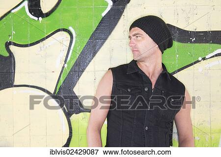 Stock Photo - Man standing in front of wall covered with graffiti. Fotosearch