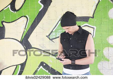 "Man standing in front of wall covered with graffiti, looking at his smartphone" View Large Photo Image Stock Photo - "Man standing in front of wall covered with graffiti, looking at his smartphone". Fotosearch