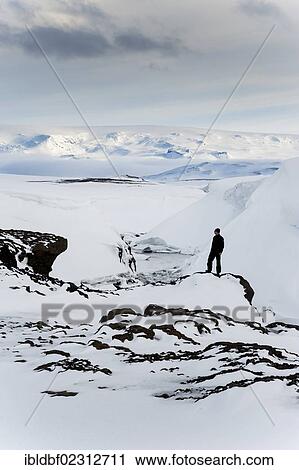 Stock Image - "Man standing on a frozen and snow-covered river, winter landscape, Vatnajoekull Glacier, Icelandic Highlands, Iceland, Europe". Fotosearch