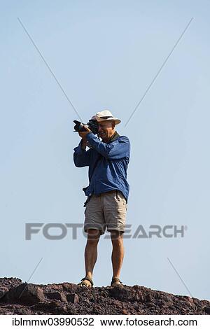 "Man taking a photo standing on a rock, Namibia, Africa" View Large Photo Image Stock Image - "Man taking a photo standing on a rock, Namibia, Africa". Fotosearch
