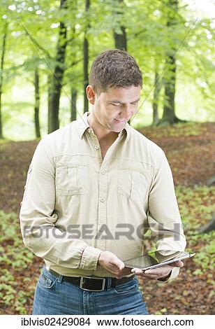 Man trekking in the woods looking at tablet pc View Large Photo Image Picture - Man trekking in the woods looking at tablet pc. Fotosearch