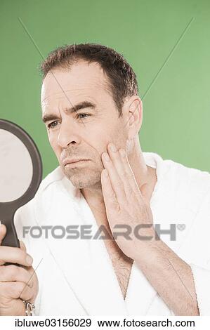 Stock Photo - "Man wearing a bathrobe observing himself critically in a hand mirror, Mannheim, Baden-Wurttemberg, Germany, Europe". Fotosearch