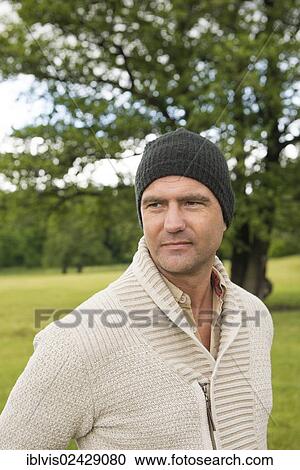 Stock Image - Man wearing a beanie standing in a park. Fotosearch