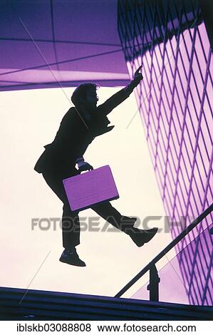 Man wearing a suit and holding a briefcase as a silhouette jumping with a hand held up in the air View Large Photo Image Stock Photo - Man wearing a suit and holding a briefcase as a silhouette jumping with a hand held up in the air. Fotosearch