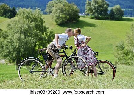 "Man wearing leather pants and a woman wearing a dirndl kissing on old bicycles within a natural landscape, Igls, Innsbruck, Tyrol, Austria, Europe" View Large Photo Image Stock Image - "Man wearing leather pants and a woman wearing a dirndl kissing on old bicycles within a natural landscape, Igls, Innsbruck, Tyrol, Austria, Europe". Fotosearch