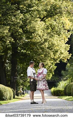 Stock Photo - "Man wearing leather pants and a woman wearing a dirndl in the Schlosspark Ambras castle gardens, Innsbruck, Tyrol, Austria, Europe". Fotosearch