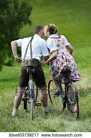 "Man wearing leather pants and a woman wearing a dirndl kissing on old bicycles within a natural landscape, Igls, Innsbruck, Tyrol, Austria, Europe" View Large Photo Image Stock Photo - "Man wearing leather pants and a woman wearing a dirndl kissing on old bicycles within a natural landscape, Igls, Innsbruck, Tyrol, Austria, Europe". Fotosearch