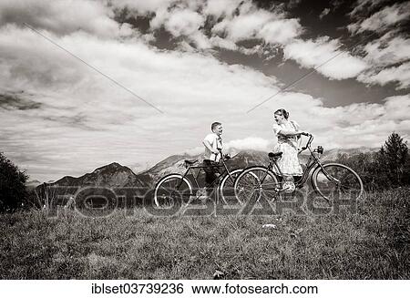 Stock Photograph - "Man wearing leather pants and a woman wearing a dirndl with old bicycles within a natural landscape, Igls, Innsbruck, Tyrol, Austria, Europe". Fotosearch
