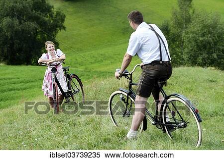 Stock Photography - "Man wearing leather pants and a woman wearing a dirndl on old bicycles within a natural landscape, Igls, Innsbruck, Tyrol, Austria, Europe". Fotosearch