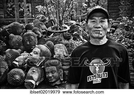 "Man with a cigar standing in front of Buddha heads made of stone, Cambodia, Asia" View Large Photo Image Stock Photo - "Man with a cigar standing in front of Buddha heads made of stone, Cambodia, Asia". Fotosearch
