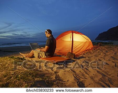 "Man with a laptop sitting in front of a tent on a sandy beach at dusk, Napali Coast, Polihale State Park, Kaua'i, Hawaii, USA" View Large Photo Image Stock Image - "Man with a laptop sitting in front of a tent on a sandy beach at dusk, Napali Coast, Polihale State Park, Kaua'i, Hawaii, USA". Fotosearch
