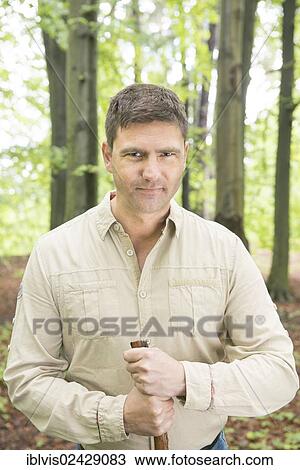 Stock Image - Man with walking stick trekking in the woods. Fotosearch