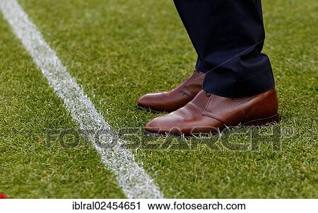 Stock Image - "Manager, detail view of fine leather shoes, standing on the edge of a football pitch". Fotosearch
