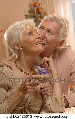 Stock Image - Mature couple exchanging gifts in front of a Christmas tree. Fotosearch