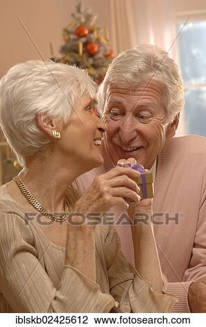 Mature couple exchanging presents in front of a Christmas tree View Large Photo Image Stock Image - Mature couple exchanging presents in front of a Christmas tree. Fotosearch