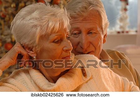 Stock Photograph - Mature couple in love sitting in front of a Christmas tree. Fotosearch