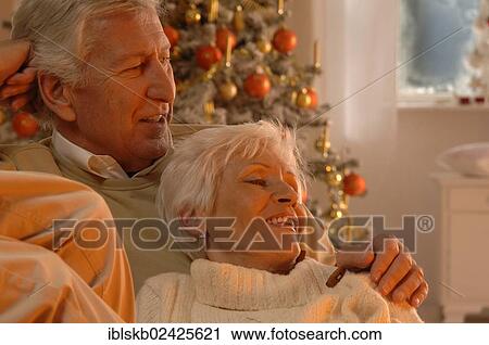 Stock Image - Mature couple in love sitting on a sofa in front of a Christmas tree. Fotosearch